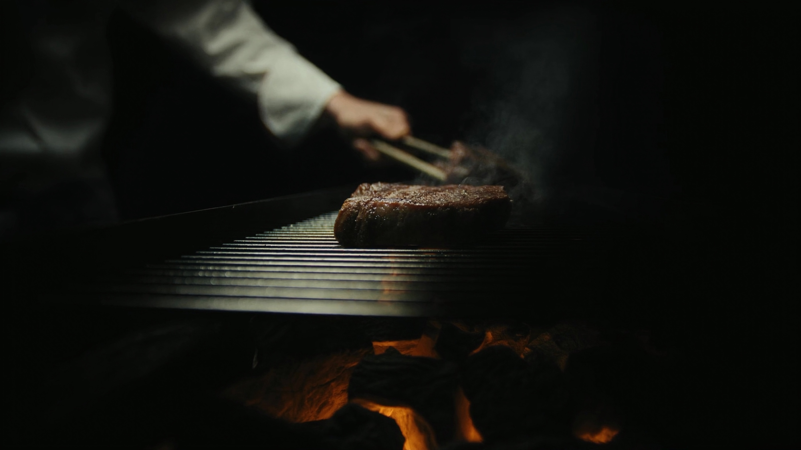 Chef virando a peça com pinça · brasa viva